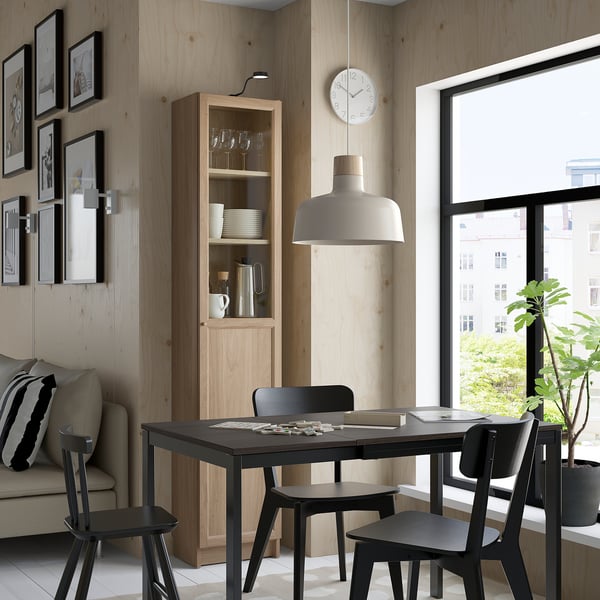 Modern dining area with black table, BILLY bookcase, pendant light, cosy sofa, and window view of greenery.
