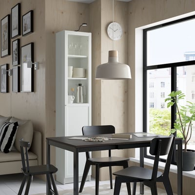 Modern dining area with BILLY white bookcase, black table, chairs, and sofa, wooden walls, hanging lamp, clock, and plant.