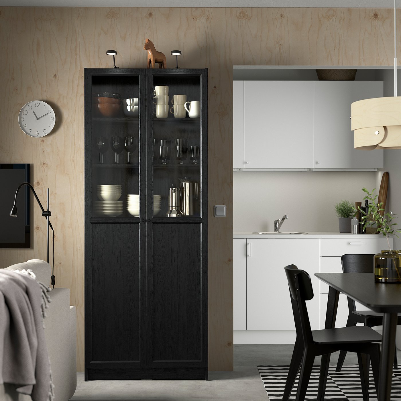 Black BILLY cabinet in minimalist kitchen, near white dining set, with glass doors showing dishes.
