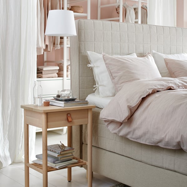 BJÖRKSNÄS bedside table, lamp, books, glass. Neutral bedding, pillows, sheer curtains. Modern scandinavian design.