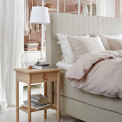 BJÖRKSNÄS bedside table, lamp, books, glass. Neutral bedding, pillows, sheer curtains. Modern scandinavian design.