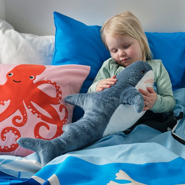 Child hugs shark toy on marine-themed bed.
