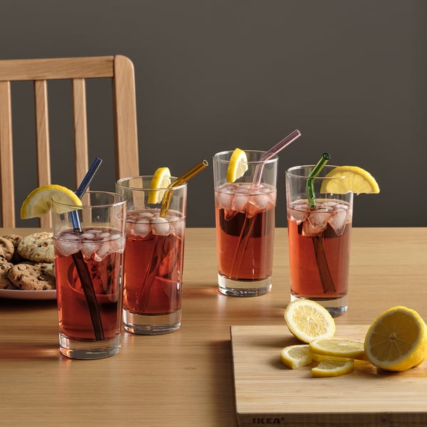 Four glasses with red iced drinks, lemon slices, and colourful glass straws on a wooden table.