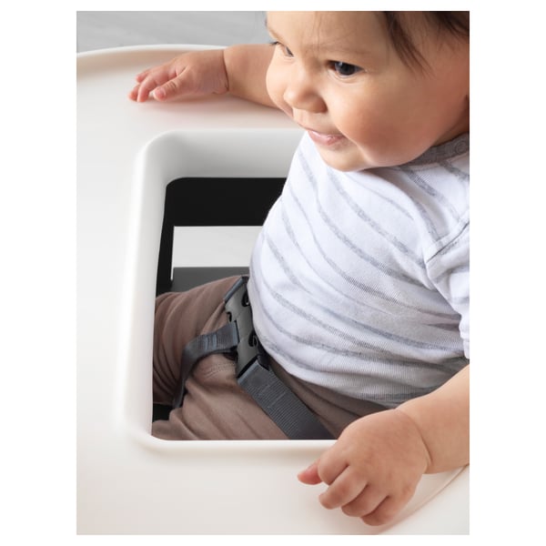 Baby in highchair with safety belt, striped shirt, brown pants.