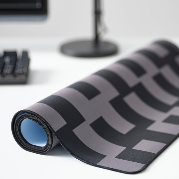 Gaming mouse pad rolled on desk, showing wide grey-black check pattern, firm surface for mouse and keyboard.
