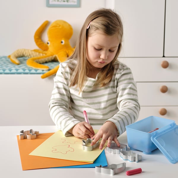 A girl uses cookie cutters and drawing on paper; a toy octopus sits nearby.