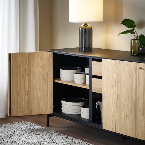 Modern sideboard with bi-fold doors and adjustable feet. Stores plates, cups, and decorative items. Wall-fastening required.