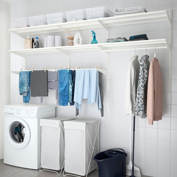 Clean, white laundry room with BOAXEL storage shelves holding clothes, cleaning supplies, and drying rack below.