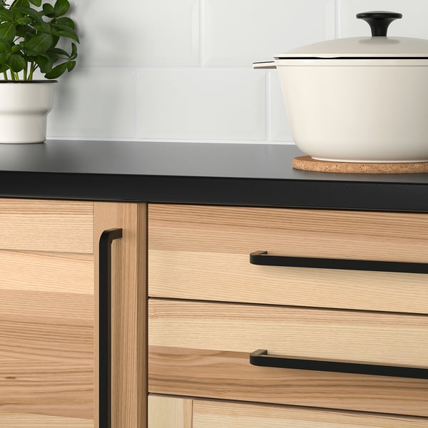 Modern kitchen drawers with light wood and black handles.