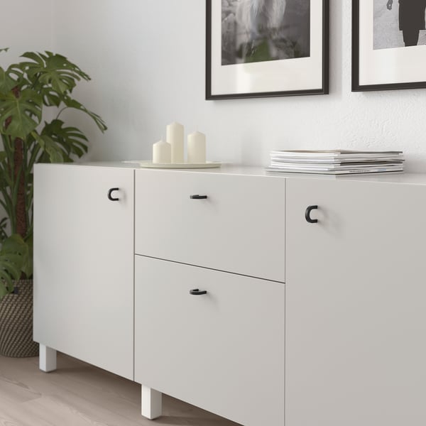 White cabinet with two doors and drawers, featuring black metal handles and legs. Decorated with candles and stacked magazines on top.