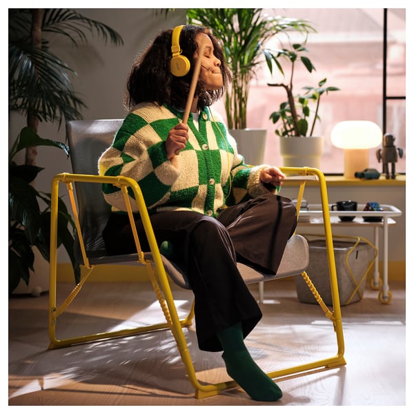 Person in BRÄNNBOLL chair, listening to music with headphones. The mesh allows airflow, and it adjusts for rocking and tilting for comfort.