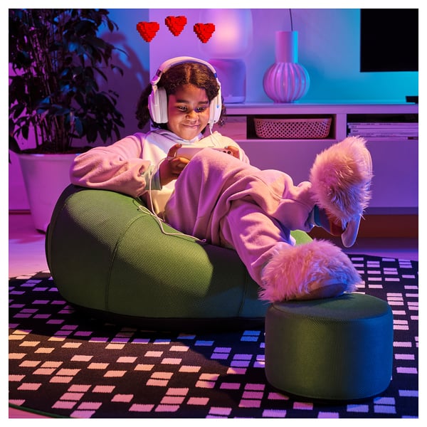 A child sits comfortably in an inflatable lounge chair, wearing headphones and playing games, with feet resting on a stool.