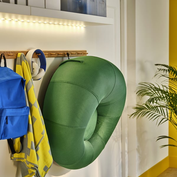 Inflated green gaming chair hangs on wall hook beside colourful backpack and sports gear. Lit shelf above.