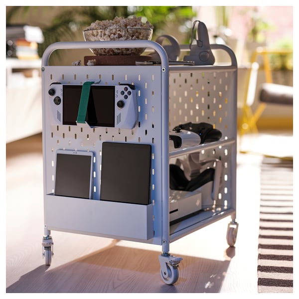 BRÄNNBOLL gaming cart, grey, metal, organised gaming gear, multiple compartments, mobile, compact, on wooden floor, striped rug nearby.