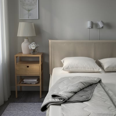 Modern bedroom with BRANDLILJA duvet on bed, bedside table, lamp, flowers. Calm, neutral colours.