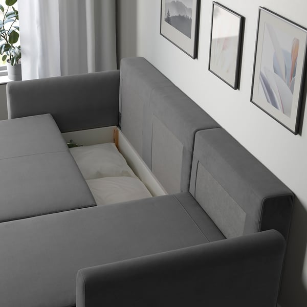 Modern grey sofa bed by BRISSUND, shown with hidden bedding compartment open, ideal for guest sleeping.