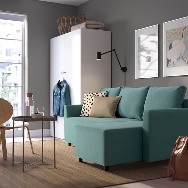Modern living room with turquoise BRISSUND sofa-bed, white storage unit, and wall art. Sofa is large, fitting near a small table and chair.