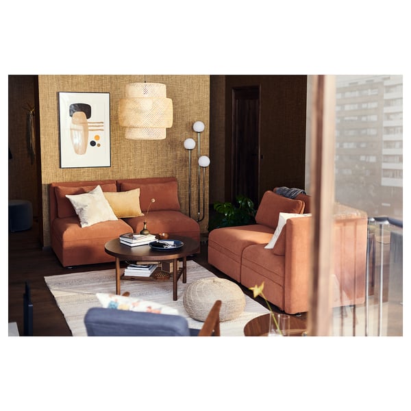 Modern living room with BRÖNDEN rug, featuring orange couches, round coffee table, hanging pendant lamp, wall art, and floor lamp.
