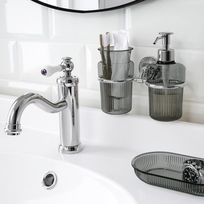 Chrome-plated sink tap with gleaming finish, accompanied by matching soap dispenser and toothbrush holder on wall, all part of brofjäreden series.