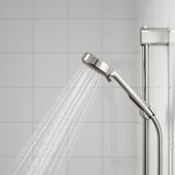 Silver shower head in use, mounted on chrome rail, releasing wide spray of water against white tiles.
