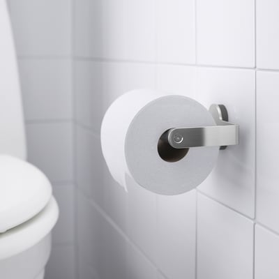 White toilet roll holder mounted on white tiled wall, holding a roll of toilet paper, part of the BROGRUND series with hidden screws.