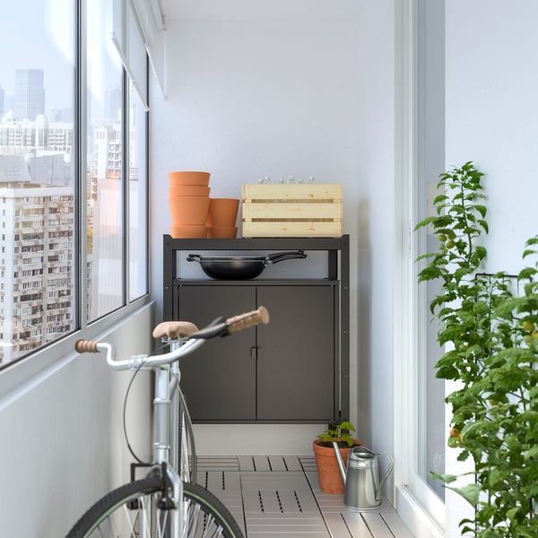 Balcony storage unit with pots, crate, bike, and plant against wall.