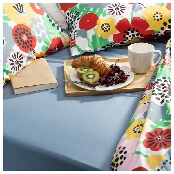 Flowery bed setup with breakfast tray, book, croissant, fruit, and coffee on a blue silk sheet.