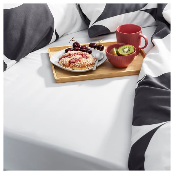 Bed tray with breakfast: pastry, cherries, kiwi. Red cup, bowl, on grey/white bedding.