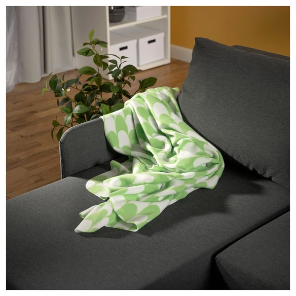 Cosy grey couch with green, white leaf-patterned throw blanket and potted plant.