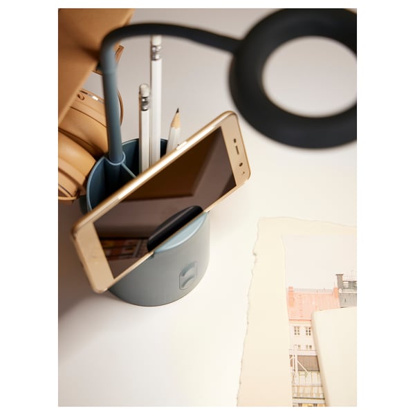 A BRUNBÅGE lamp, grey, holding a phone and pens, with a black headphone. Perfect for a tidy workspace.
