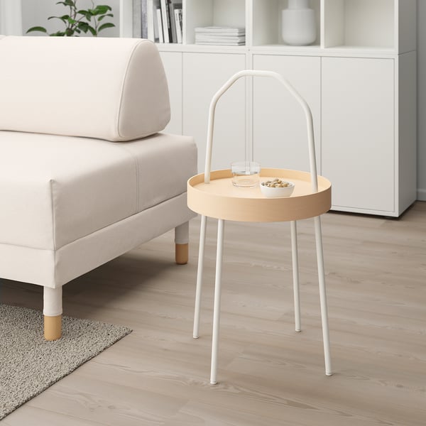 Round BURVIK side table with birch top & white legs beside sofa & bookshelf.