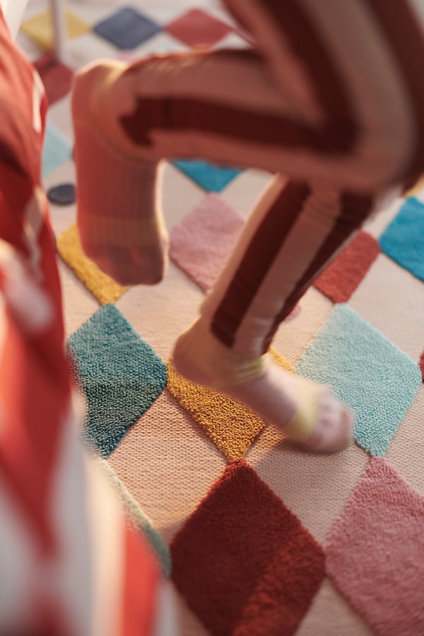 Child plays on colourful BUSENKEL rug with geometric pattern.