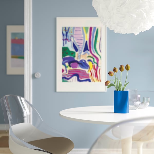 A modern dining area a small blue vase with tulips on a white table. Nearby, a colourful abstract painting adds vibrancy to the light blue wall.