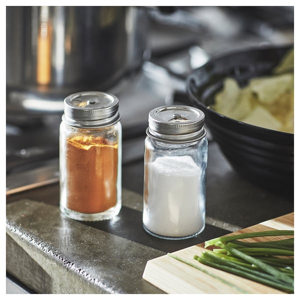 Two spice jars with silver lids on a countertop, one filled with brown spice, the other with white salt.