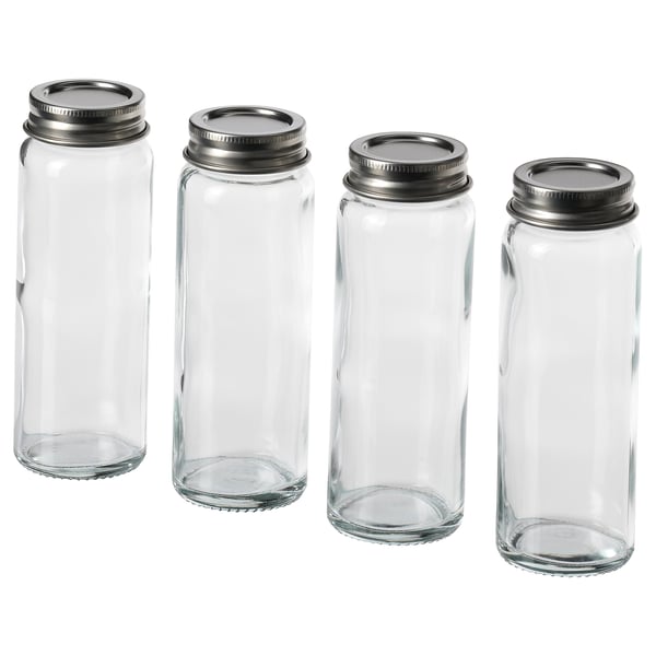 Four clear, cylindrical glass jars with silver metal lids, standing upright in a row.