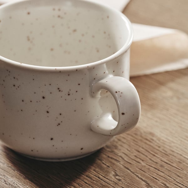 Cup on wooden table, light beige with dark spots, quality speckled design.
