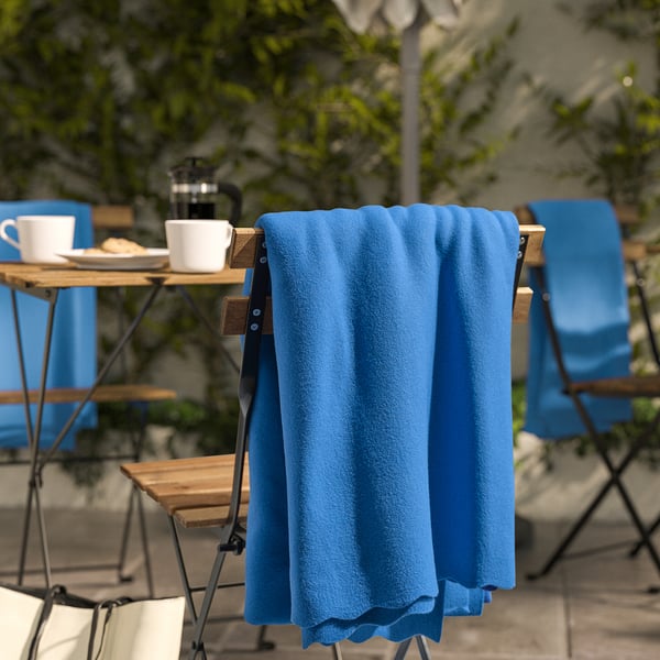 Blue fleece blanket draped on chair near outdoor café setup with cups and table.