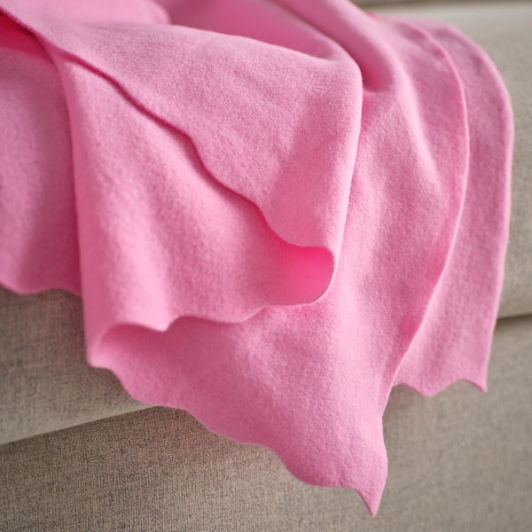 Bright pink, soft fleece blanket draped over a beige surface, showing its cosy texture and inviting warmth.