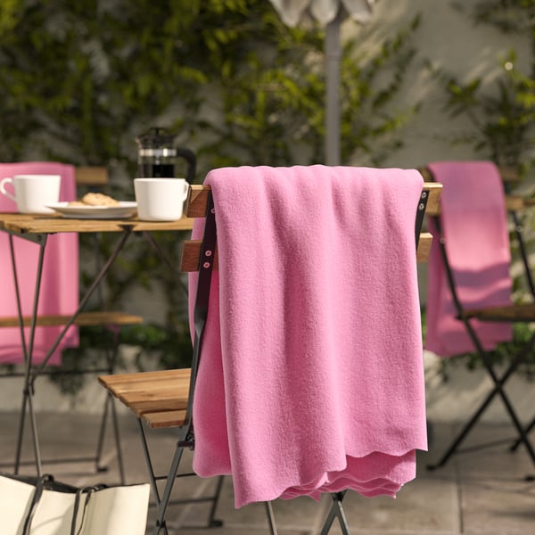 Pink fleece blanket DAGGKÅPOR draped on chair, larger than cups & plates on table.