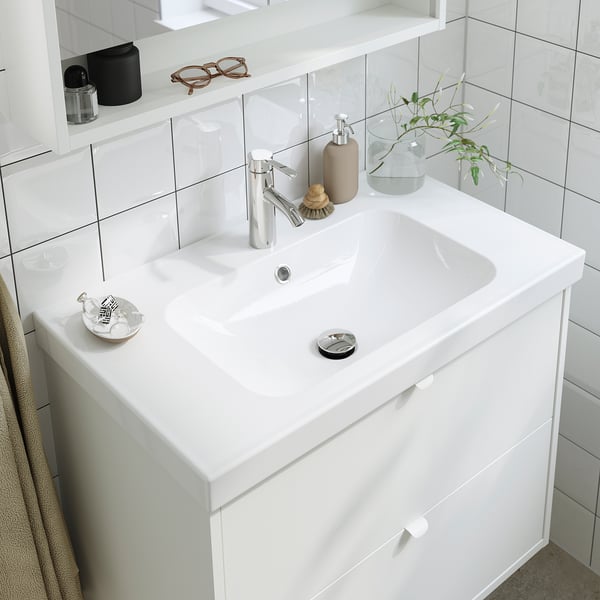 White bathroom sink with chrome mixer tap, featuring cold start function. Small dish, soap dispenser, and plant on counter.