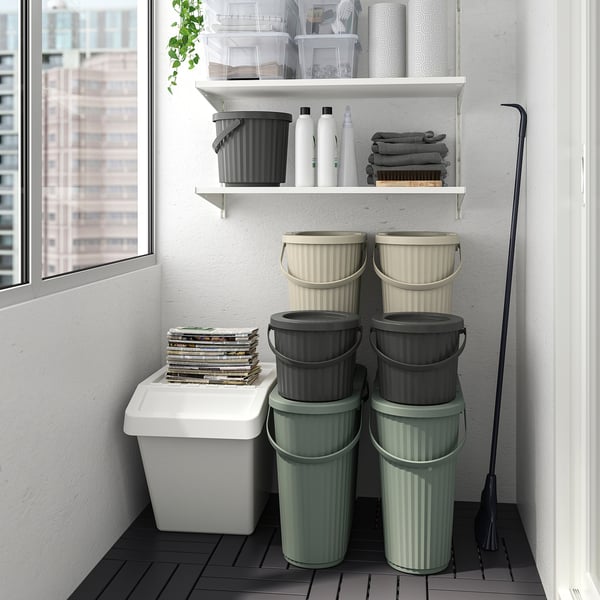 Stacked green and grey DAMMÄNG bins near window, with a white magazine bin and broom. Organised waste sorting setup.
