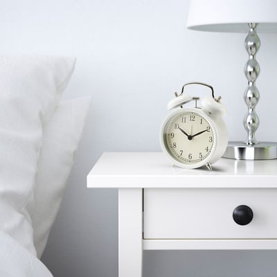 White alarm clock on bedside table with modern quartz movement, no ticking sound.