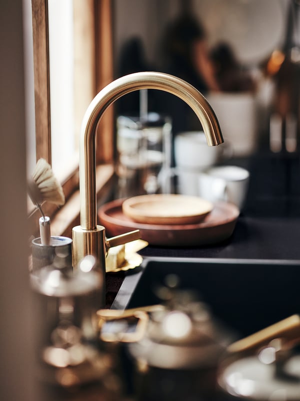 Gold-colored kitchen tap with sleek, curved design and brass material, positioned on a dark countertop.