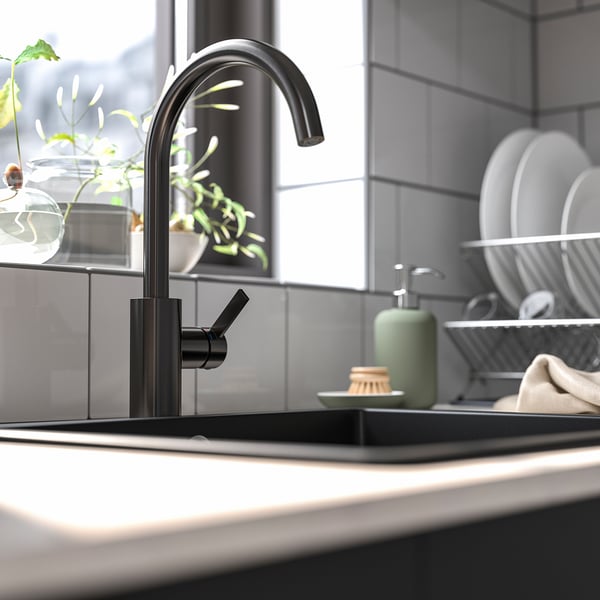 Modern black kitchen tap with high arc spout, sleek design, positioned near sink, surrounded by plates and soap dispenser.