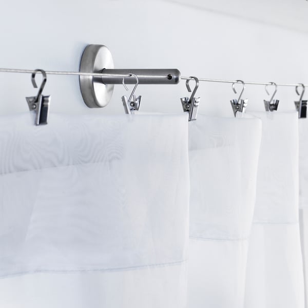 Stainless steel curtain rod with adjustable angle fittings, supporting white curtains.