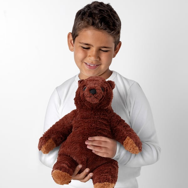 A boy wearing a white shirt holds a soft brown teddy bear, suitable for children from 12 months.