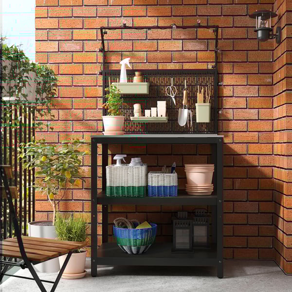 Black metal gardening shelf with tools, pots, baskets, against brick wall.