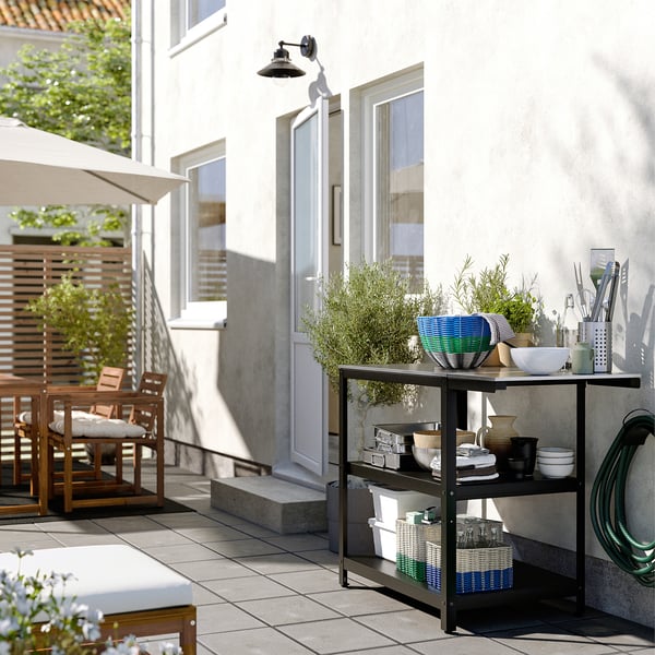 Modern, outdoor scene with DJURTRÄNARE baskets on a stand. Baskets in black/white, round, storing items on patio.