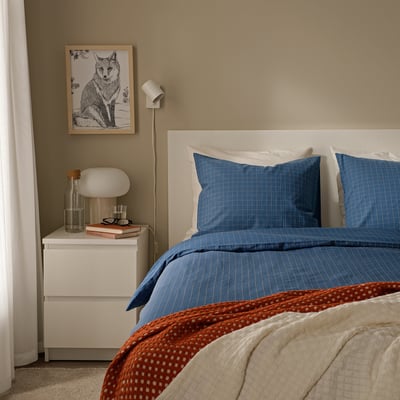 Cosy bedroom with DOFTAKLEJA dark blue check duvet, white bed, red polka dots, bedside table with lamp, books, plant, fox picture, calm colours.