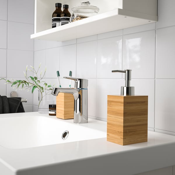 Modern bathroom sink with DRAGAN dispenser. White counter, chrome fixtures, light wood box, clear acrylic dispenser.